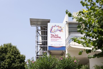 Large billboard signage at the Thessaloniki event space that reads 'The Art of Healing'